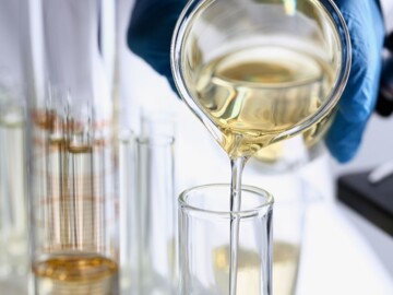 Hand mit blauem Handschuh gießt gelbe Flüßigkeit in Reagenzglas