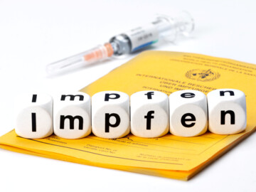 Gelbes Impfheft, Spritze und das Wort „Impfen“ aus Würfeln gebildet