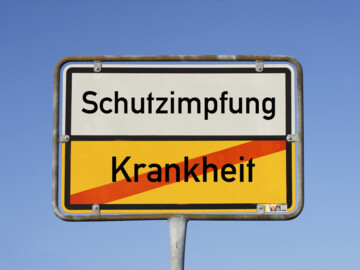 Ortsschild: Aufschrift oben „Schutzimpfung“, unten durchgestrichen „Krankheit“