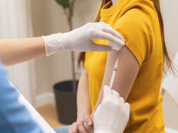 Eine Frau in einem gelben Pullover, die eine Grippeimpfung in der Arm erhält
