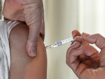 Spritze mit Impfstoff wird in den Oberarm gestochen