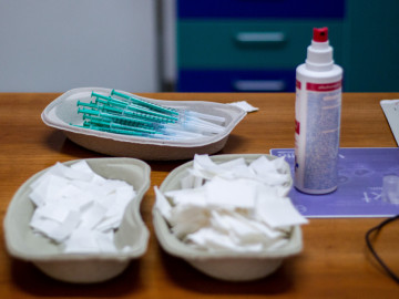 Aufgezogene Spritze mit Impfstoff in einer Pappschale, davor Mulltupfer und eine Flasche Desinfektionsmittel