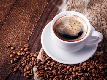 Tasse mit dampfendem Kaffee umgeben von Kaffeebohnen