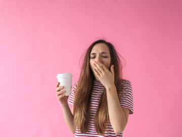 Junge Frau mit Coffee-to-go-Becher in der Hand gähnt