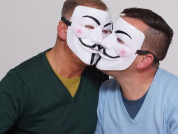 Zwei Männer Wange an Wange mit Masken vor dem Gesicht.