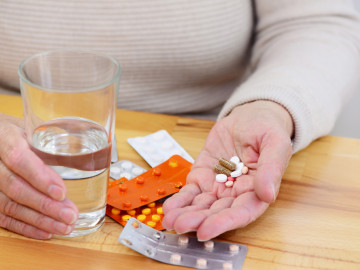 Frau mit einem Glas Wasser und Tabletten in der Hand