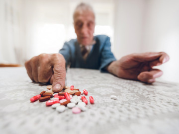 Senior zeigt auf einen Haufen von Medikamenten, die auf dem Tisch liegen