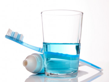 Glas mit blauem Mundwasser und dahinter Zahnbürste und Zahnpasta