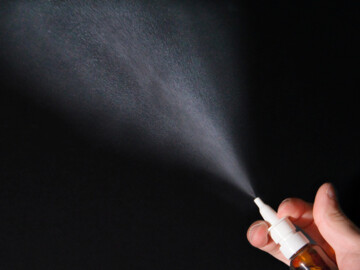 Hand sprüht Nasenspray vor schwarzem Hintergrund