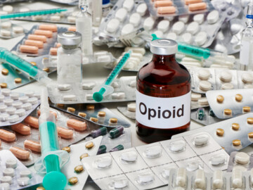 Eine Ampulle Opioid, welche umgeben ist von Tabletten, Verpackungen und Spritzen sowie anderen Ampullen