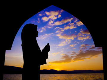 Silhouette einer muslimischen Frau, die während des Sonnenuntergangs in einer Moschee betet