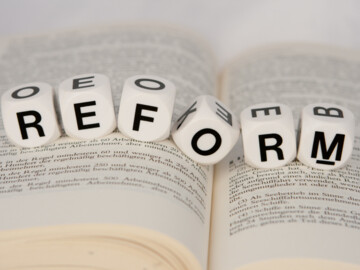 Aufgeschlagenes Buch und Wort „Reform“ aus Würfeln darübergelegt
