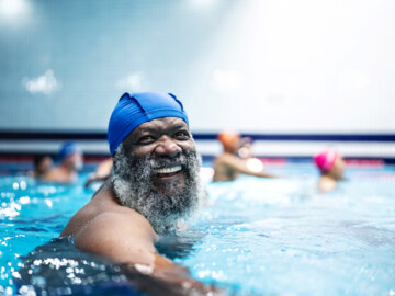 Älterer Mann mit grauem Bart und blauer Badekappe im Schwimmbad