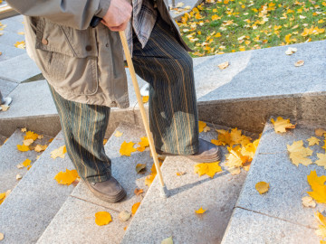 Alter Mann mit Gehstock steigt mit Laub bedeckte Treppen hoch