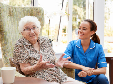 Seniorin im Sessel neben eine Pflegekraft