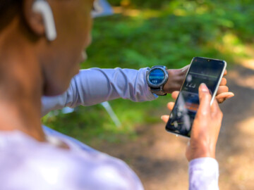Joggerin blickt auf Handy und Smartwatch
