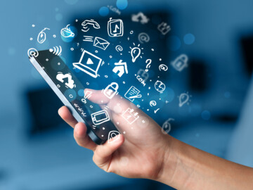 Viele Icons und Symbole umschwirren ein Smartphone, dass eine Person in der Hand hält.