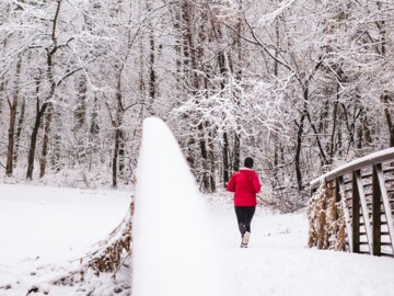 Mann mit roter Jacke joggt über eine verschneite Brücke in Richtung Wald