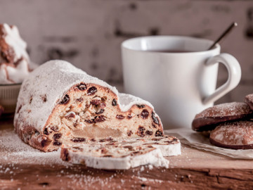 Angeschnittener Weihnachtsstollen mit einer Tasse Kaffee, Zimtsternen und Lebkuchen im Hintergrund
