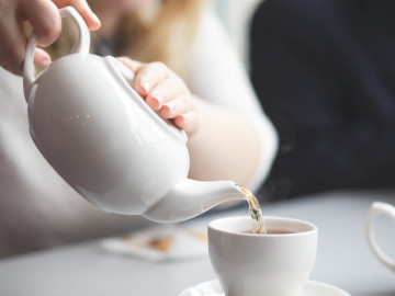 Frau schenkt Tee aus der Teekanne in eine Tasse