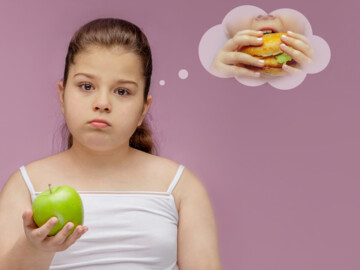Mädchen mit traurigem Gesicht hält grünen Apfel in der Hand und denkt daran, in einen Burger zu beißen.