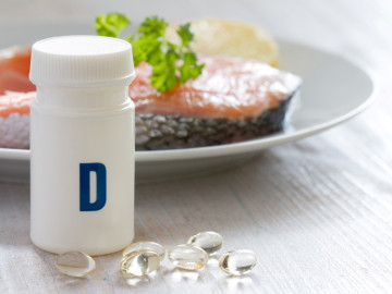 Lachssteak auf einem Teller, im Vordergrund Vitamin-D-Supplemente