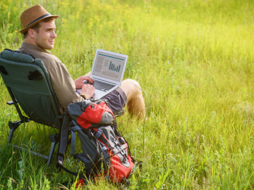 Wanderer im Liegestuhl auf einer Wiese mit Laptop auf dem Schoss