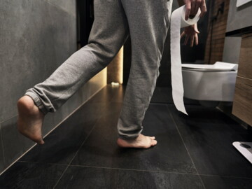 Person geht mit Toilettenpapierrolle in der Hand zum WC.