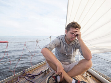 Mann ist seekrank auf einem Segelboot.