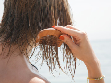 Frau kämmt sich die feuchten Haare am Strand.