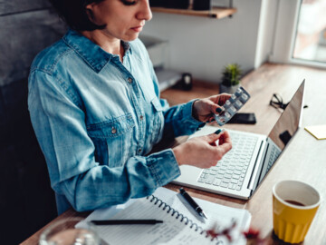 Frau mit Tabletten und Kaffee am Laptop
