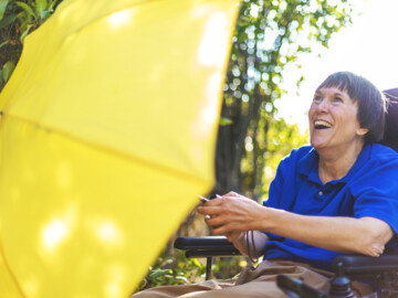 Frau im Rollstuhl mit gelbem Regenschirm