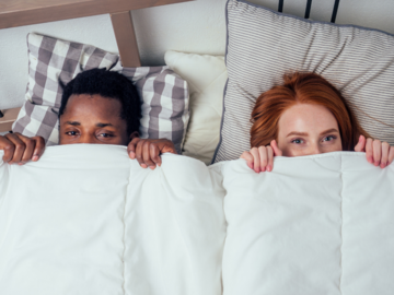 Mann und Frau ziehen sich Bettdecke bis unter die Augen