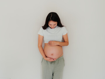 Schwangere Frau hält sich den unbedeckten Bauch.