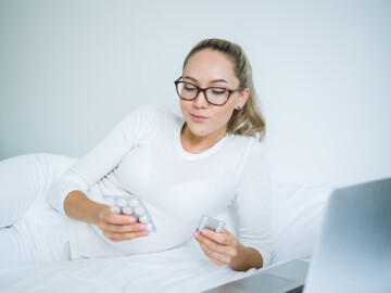 Frau liegt mit Vitamintabletten in den Händen auf dem Sofa